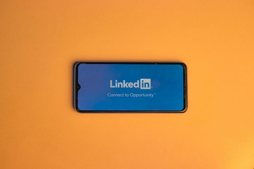 Smartphone showing LinkedIn login on vibrant orange background, symbolizing connectivity. Standout LinkedIn Profile