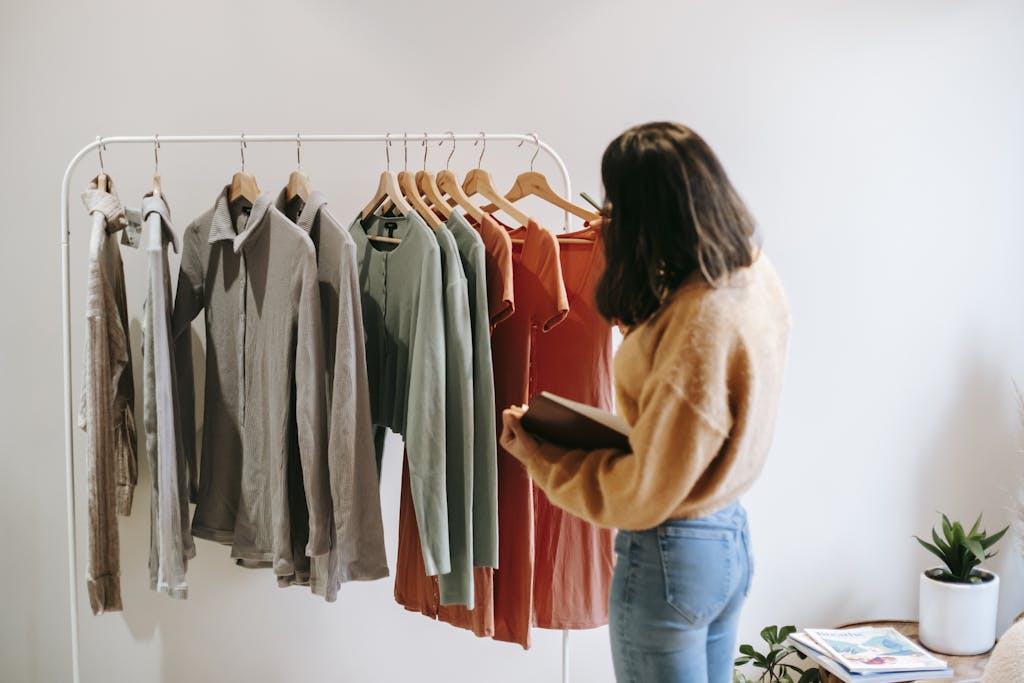 A woman selects garments from a rack in a cozy boutique, holding a notepad.