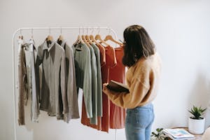 A woman selects garments from a rack in a cozy boutique, holding a notepad.