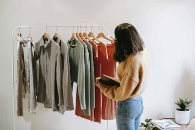 Colors Meaning in Headshots – What Your Outfit Says About You 15 A woman selects garments from a rack in a cozy boutique, holding a notepad.