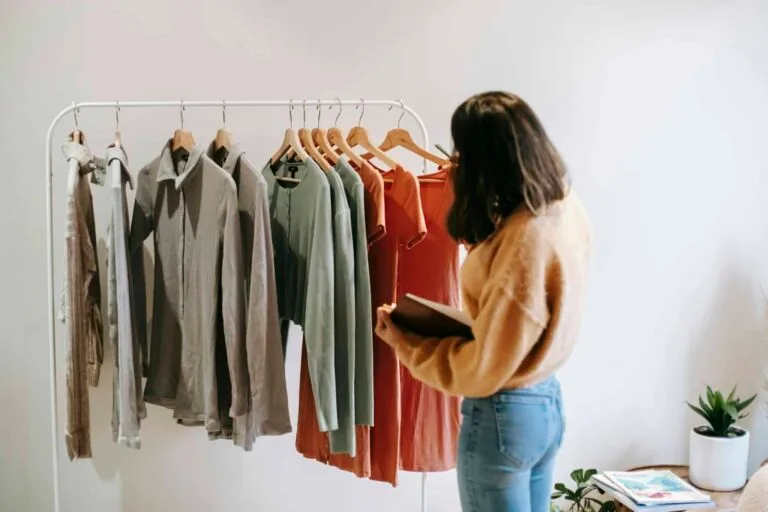 Colors Meaning in Headshots – What Your Outfit Says About You 1 A woman selects garments from a rack in a cozy boutique, holding a notepad.
