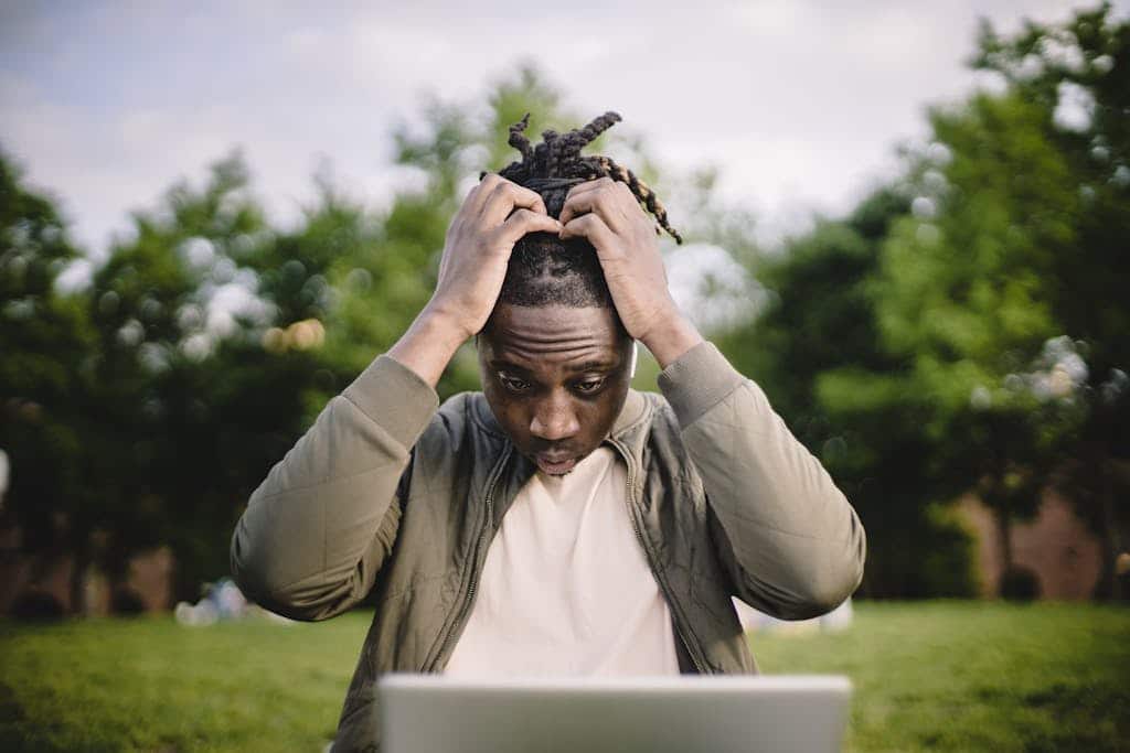 Professional Headshot Mistakes Upset young African American male freelancer clutching head with hands after failure in project while working remotely in park
