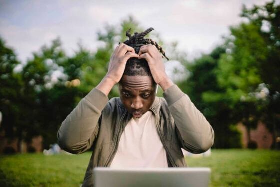 Professional Headshot Mistakes Upset young African American male freelancer clutching head with hands after failure in project while working remotely in park