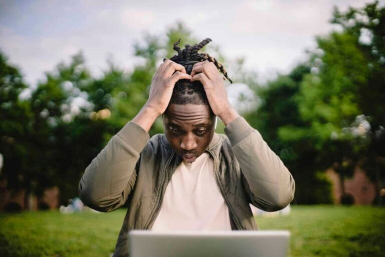 Professional Headshot Mistakes Upset young African American male freelancer clutching head with hands after failure in project while working remotely in park