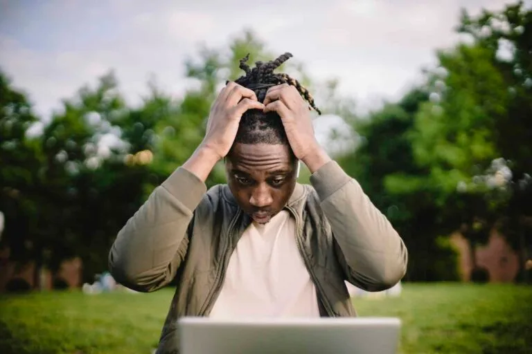 Professional Headshot Mistakes Upset young African American male freelancer clutching head with hands after failure in project while working remotely in park