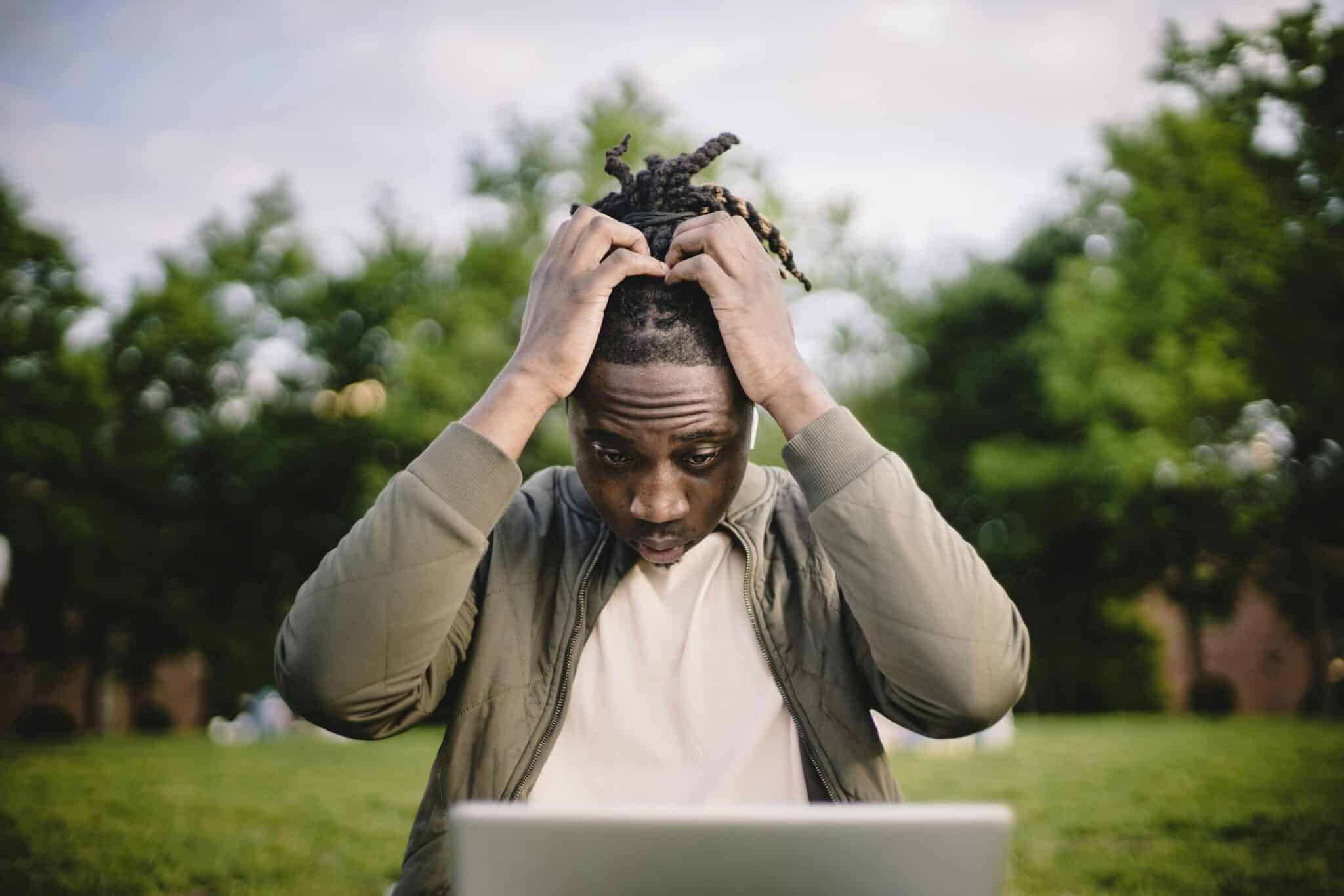 Professional Headshot Mistakes Upset young African American male freelancer clutching head with hands after failure in project while working remotely in park