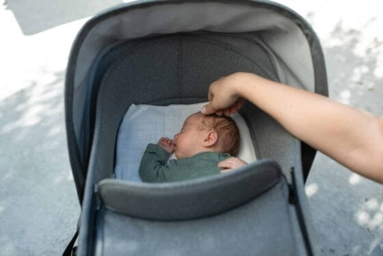 Travel Systems vs Modular Strollers | A serene moment of a baby sleeping in a stroller with a gentle touch from an adult hand.