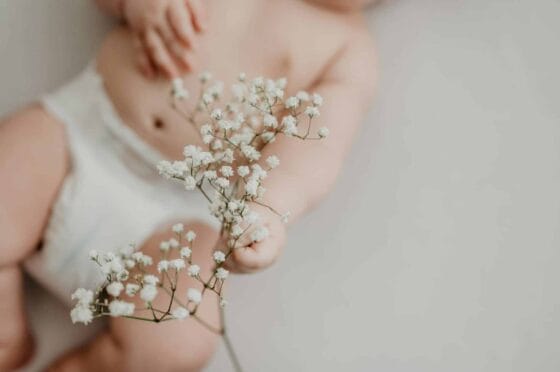 diapering survival guide | Portrait of a baby in a diaper delicately holding white flowers, emphasizing innocence.