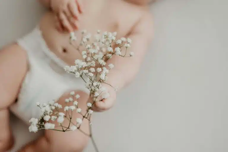 Diapering Survival Guide: 7 Smart Tips Every Parent Should Know 8 diapering survival guide | Portrait of a baby in a diaper delicately holding white flowers, emphasizing innocence.