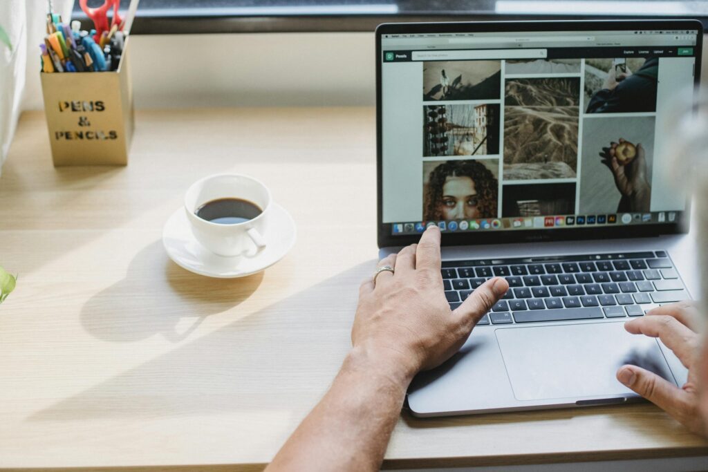 Crop anonymous male searching photos on internet using netbook while drinking coffee at table | Brand Photos vs Stock Photos