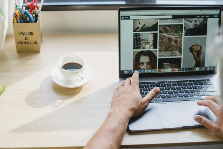 Crop anonymous male searching photos on internet using netbook while drinking coffee at table | Brand Photos vs Stock Photos