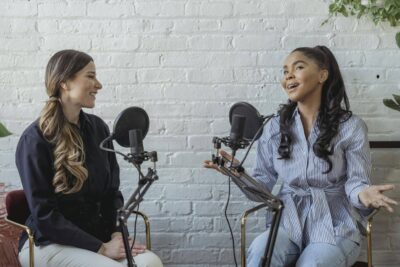 Best Personal Branding Photos for Speaking, Media & Podcasts 76 Personal branding photos for media Smiling African American female guest gesticulating while having interview with journalist sitting near mic