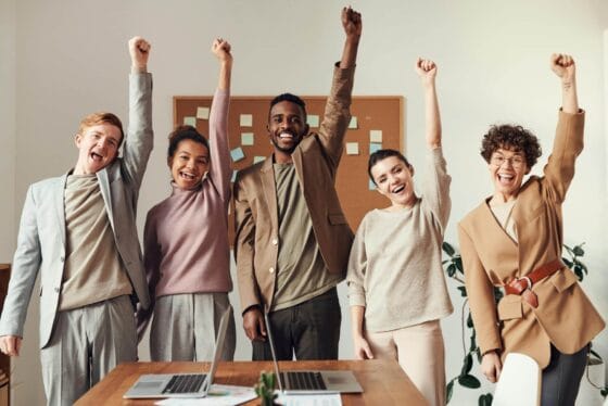 professional headshots for real estate teams A diverse team celebrating success with raised hands in a modern office setting.