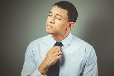 The #1 Personal Branding Photo Mistake People Make (and How to Avoid It) 89 A man indoors adjusting his necktie with a thoughtful expression, wearing formal attire. Personal Branding Photo Mistake