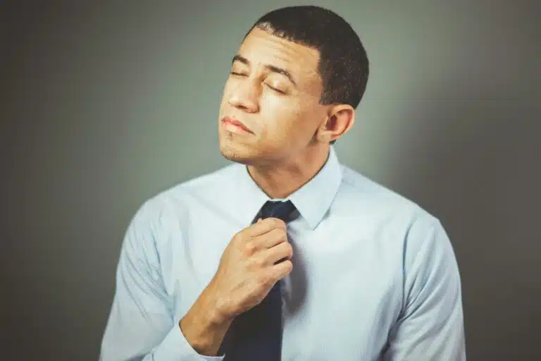 A man indoors adjusting his necktie with a thoughtful expression, wearing formal attire. Personal Branding Photo Mistake