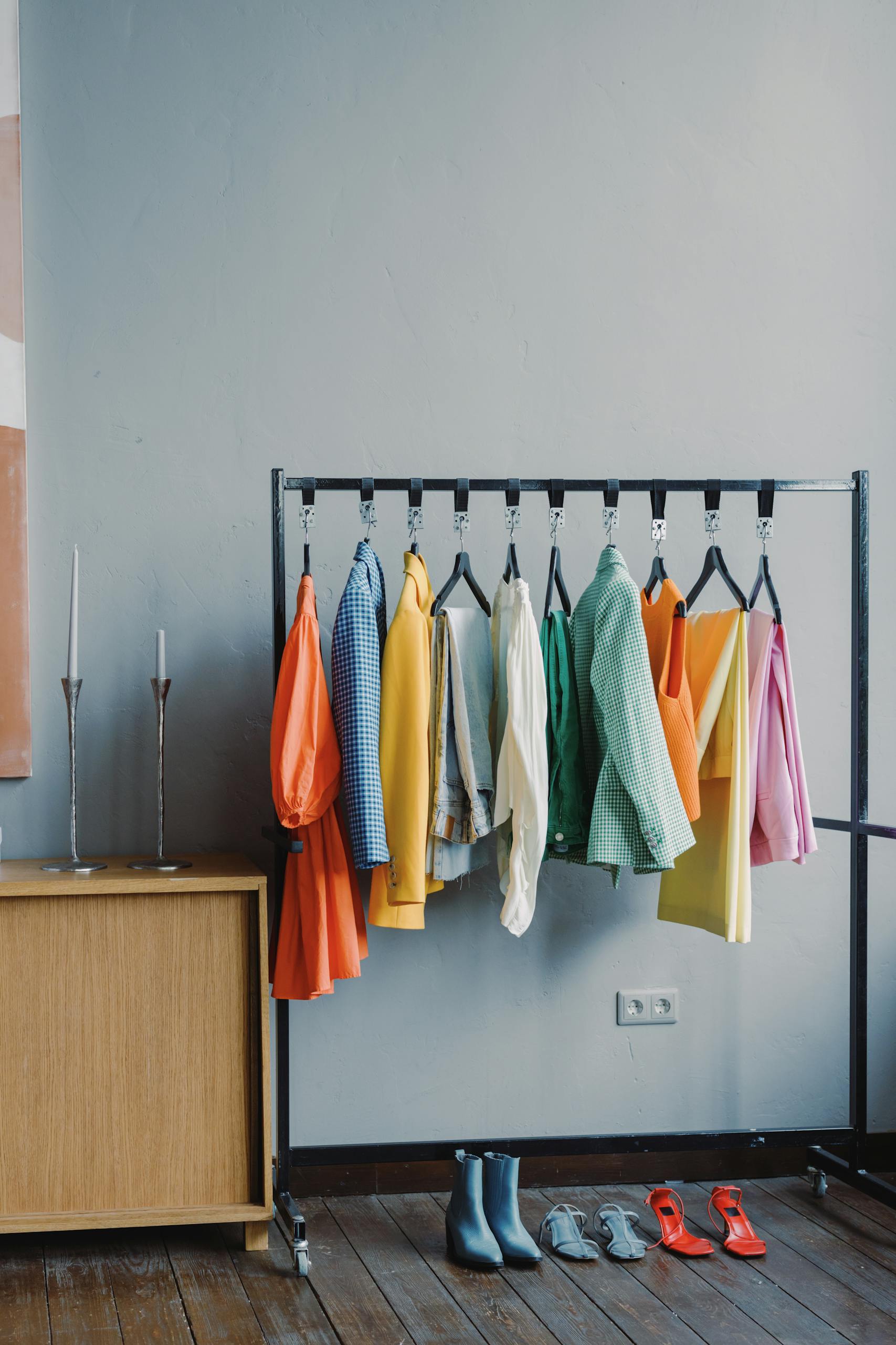 branding session outfit changes A vibrant clothes rack with colorful outfits in a minimalist room setting.