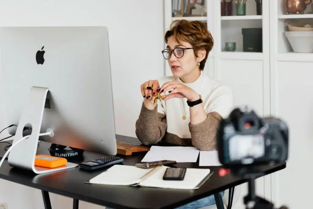 CRM for photographers A professional woman engaged in a virtual meeting setup at her home desk, using a computer and camera.