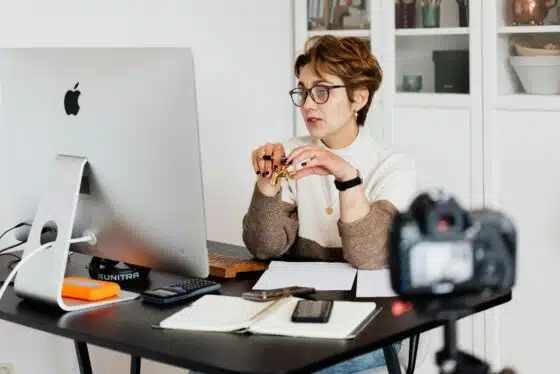 CRM for Photographers: What to Look For 93 CRM for photographers A professional woman engaged in a virtual meeting setup at her home desk, using a computer and camera.