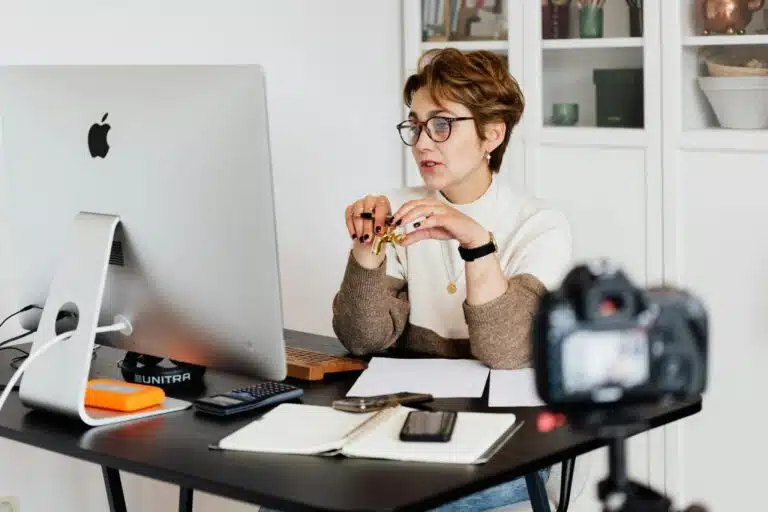 CRM for photographers A professional woman engaged in a virtual meeting setup at her home desk, using a computer and camera.