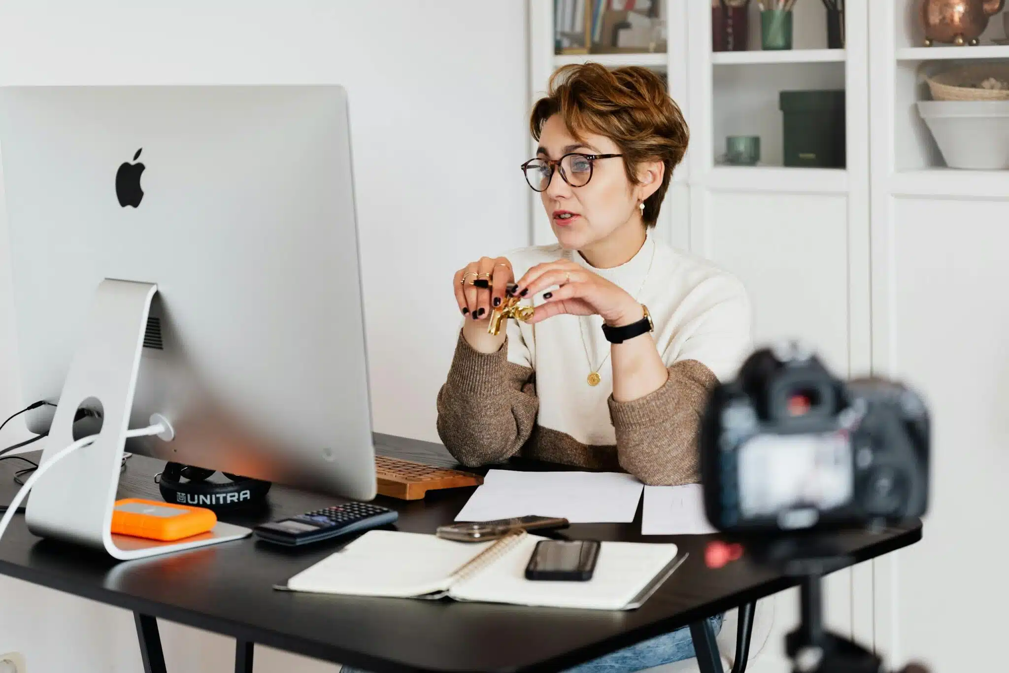 CRM for Photographers: What to Look For 12 CRM for photographers A professional woman engaged in a virtual meeting setup at her home desk, using a computer and camera.