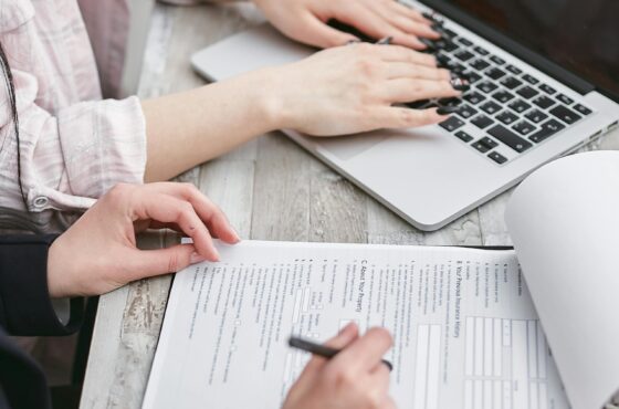 Go High Level vs HoneyBook Close-up of hands typing on a laptop and reviewing business documents, focused on finance and legal tasks.