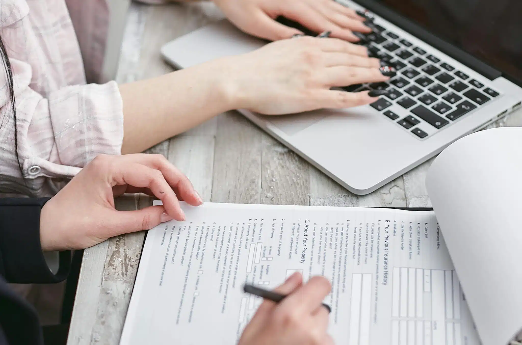 Go High Level vs HoneyBook Close-up of hands typing on a laptop and reviewing business documents, focused on finance and legal tasks.