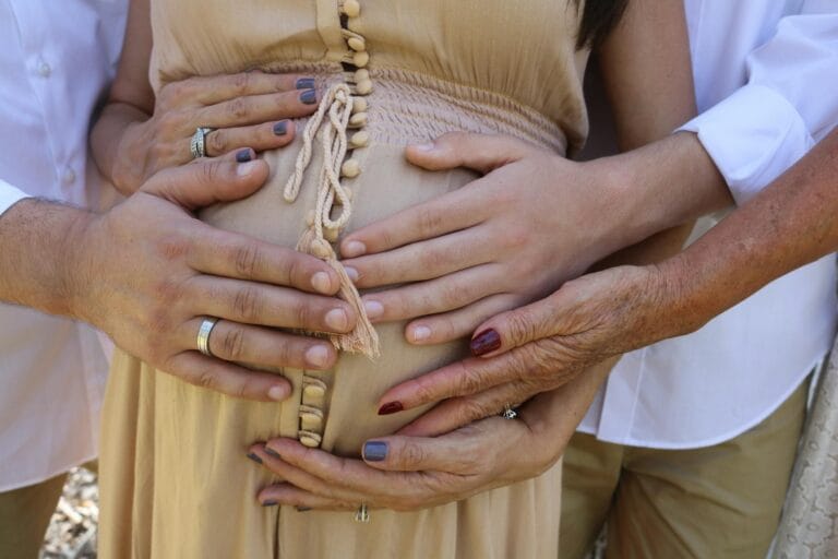 Close-up of family hands touching a pregnant belly, symbolizing love and support during pregnancy. Maternity Sessions With Grandma