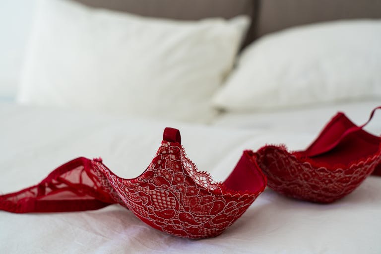 A red lace bra elegantly laid on a white bed in a stylish bedroom setting. Boudoir Outfit Mistakes