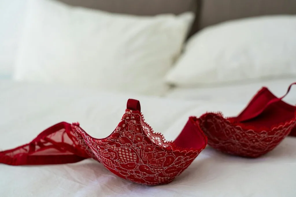 Boudoir Outfit Mistakes: 5 Critical Pitfalls (and How to Avoid Them) 4 A red lace bra elegantly laid on a white bed in a stylish bedroom setting. Boudoir Outfit Mistakes