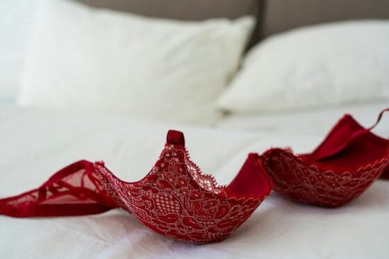 A red lace bra elegantly laid on a white bed in a stylish bedroom setting. Boudoir Outfit Mistakes