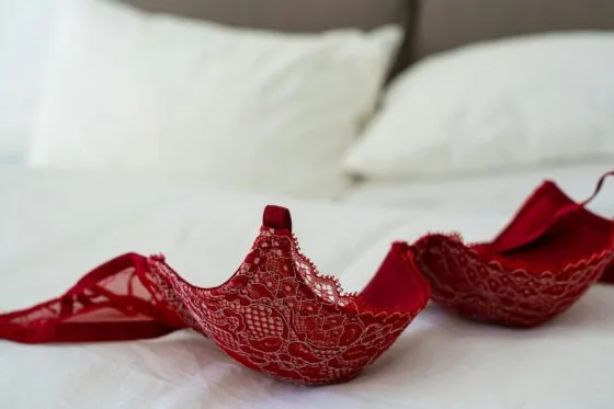 A red lace bra elegantly laid on a white bed in a stylish bedroom setting. Boudoir Outfit Mistakes
