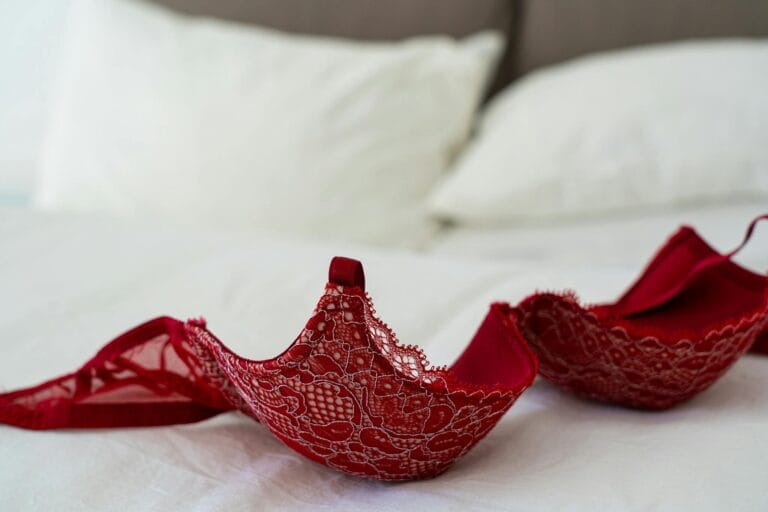 A red lace bra elegantly laid on a white bed in a stylish bedroom setting. Boudoir Outfit Mistakes