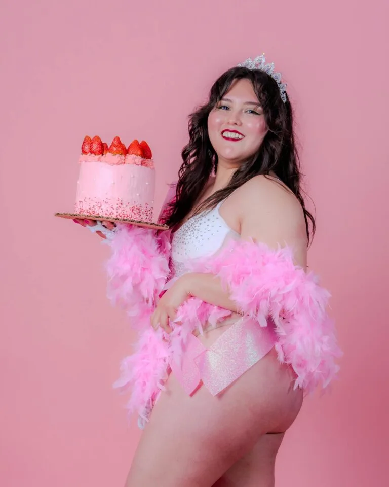 Birthday boudoir photoshoot Happy woman in a festive attire holding a pink cake on a vibrant backdrop.
