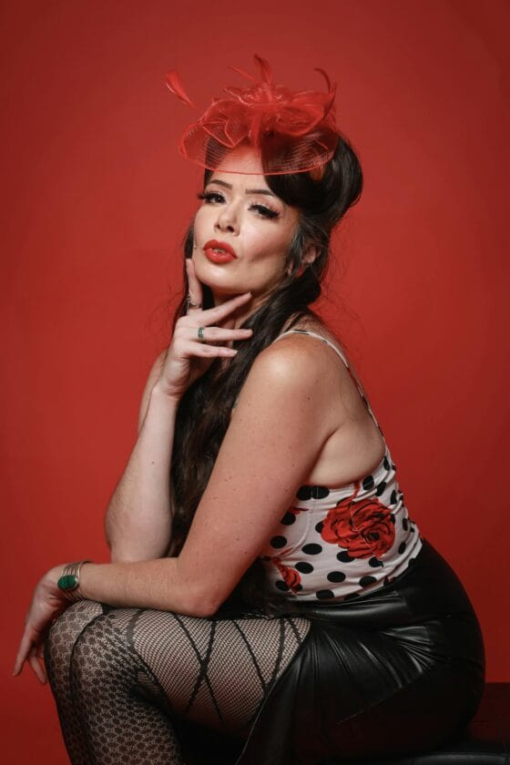 Vintage inspired boudoir photography Elegant portrait of a vintage pinup style model with red accents and floral patterns on a studio backdrop.