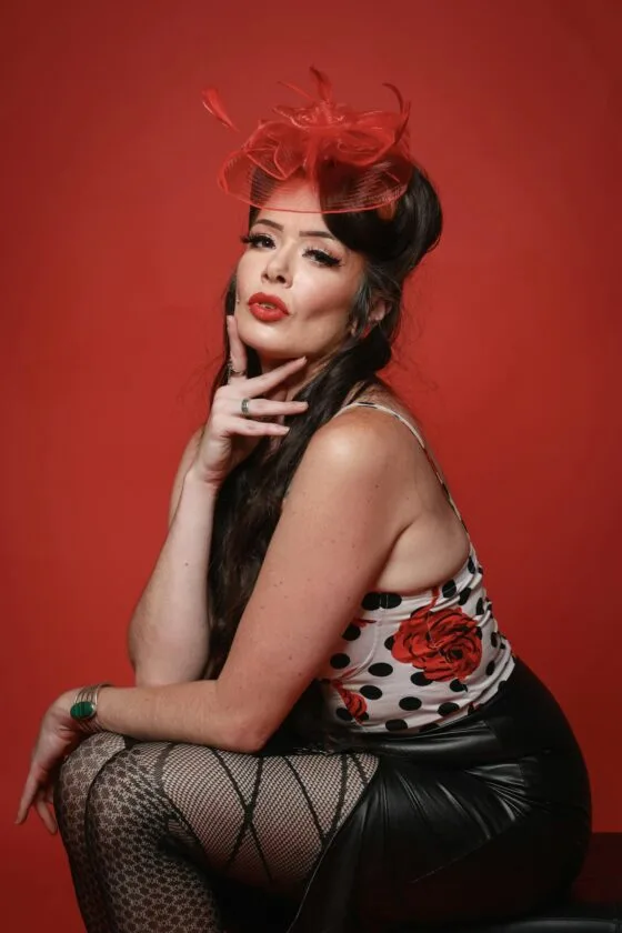 Vintage inspired boudoir photography Elegant portrait of a vintage pinup style model with red accents and floral patterns on a studio backdrop.