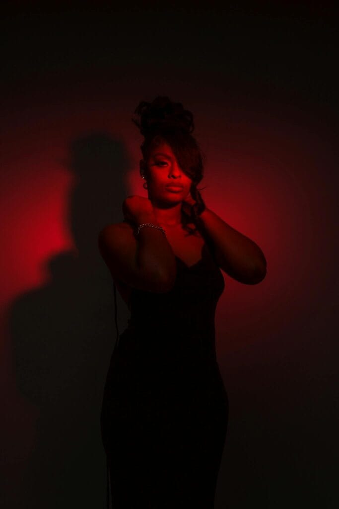 Celebrating Women of Color Boudoir A striking portrait of an elegant woman in a black dress, highlighted by dramatic red lighting.