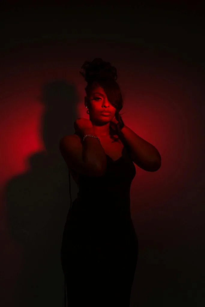 Celebrating Women of Color Boudoir A striking portrait of an elegant woman in a black dress, highlighted by dramatic red lighting.
