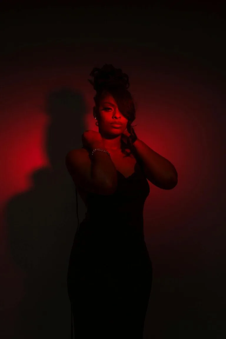 Celebrating Women of Color Boudoir A striking portrait of an elegant woman in a black dress, highlighted by dramatic red lighting.